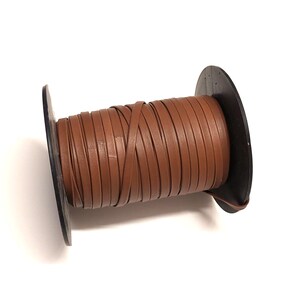 Könnte beinhalten: Eine Spule mit braunem Lederband, das um eine schwarze Kunststoffspule gewickelt ist. Das Band ist etwa 6 mm breit.
