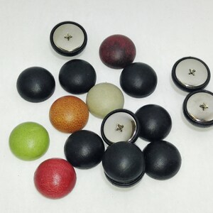 Peut inclure: Assortiment de boutons ronds de différentes couleurs et textures, notamment noir, marron, vert, rouge et beige. Certains boutons ont une finition métallique.