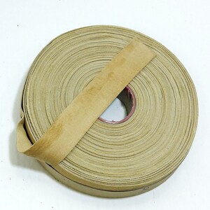 May include: A roll of brown paper tape with a tan colored backing. The tape is wound around a cardboard core.