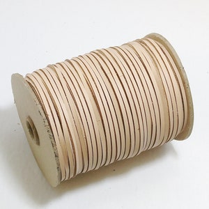 Może przedstawiać: Szpula jasnobeżowego sznurka skórzanego. Sznurek jest ciasno nawinięty na szpulę kartonową.