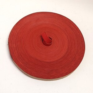 Op de afbeelding: Een rol rood lederen koord, opgerold tot een cirkel. Het koord is ongeveer 1,2 cm breed.