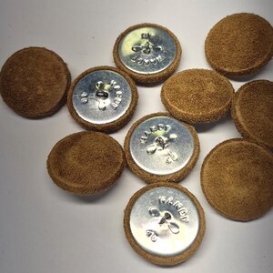May include: A collection of round buttons featuring a textured brown suede-like fabric covering the top surface. The underside of each button is made of polished silver-colored metal with a central shank and the embossed text HANDY CO.