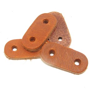 Puede incluir: Cuatro correas de cuero marr&oacute;n con dos agujeros cada una. Las correas son de forma ovalada y tienen una textura rugosa.