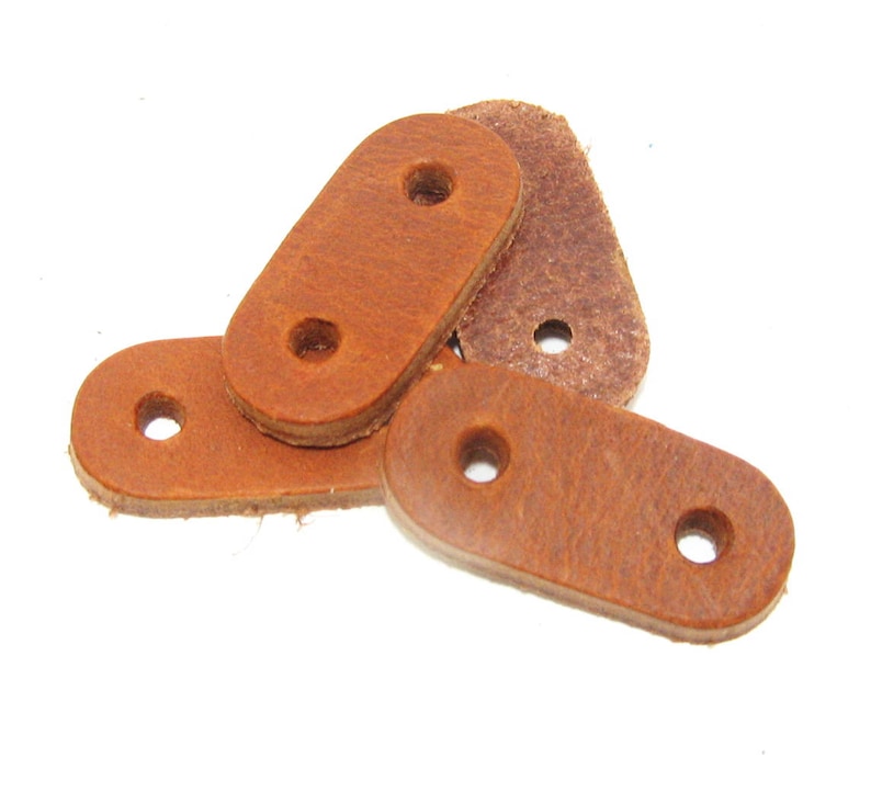 Puede incluir: Cuatro correas de cuero marr&oacute;n con dos agujeros cada una. Las correas son de forma ovalada y tienen una textura rugosa.