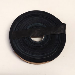 Puede incluir: Un rollo de cinta de tela negra, enrollado apretadamente y asegurado con una banda negra.