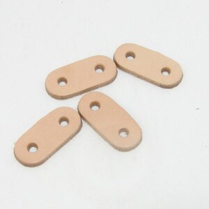 Puede incluir: Cuatro correas de cuero marr&oacute;n claro con dos agujeros cada una. Las correas son de forma ovalada y tienen una textura lisa.