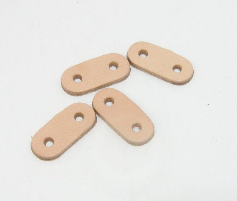 Puede incluir: Cuatro correas de cuero marr&oacute;n claro con dos agujeros cada una. Las correas son de forma ovalada y tienen una textura lisa.