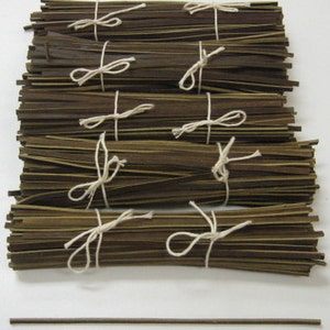 Puede incluir: Una pila de tiras de material marrón y dorado atadas con cuerda blanca. Las tiras están dispuestas en una pila ordenada y todas son del mismo tamaño. Hay una sola tira delgada del mismo material en la parte inferior de la imagen.