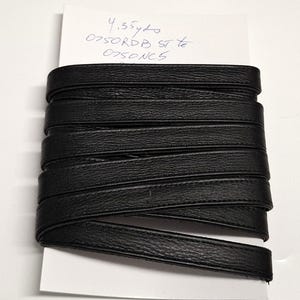 May include: A roll of black leather trim, approximately 4.35 yards in length, is displayed on a white background. The trim is tightly wound, showcasing its textured surface and dark color. The image includes handwritten text on a small white paper.