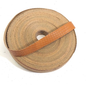 Może przedstawiać: Rolka brązowej taśmy korkowej z brązową skórzaną lamówką. Taśma jest zwinięta, a lamówka owinięta wokół rolki.