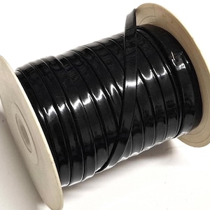 May include: A spool of glossy black flat cord wrapped tightly around a beige plastic reel. The cord has a smooth, reflective surface and is wound in uniform, side-by-side rows across the entire width of the cylindrical spool core.