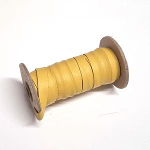 May include: A spool of yellow leather cord wrapped around a cardboard core.