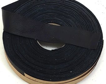 May include: A roll of black leather cord or strip featuring a textured surface. The material is wound into a circular coil, with one end extending outward. The underside of the strip shows a tan-colored adhesive backing along the edge.