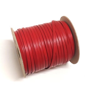 May include: A spool of red leather cord. The cord is wound tightly around a cardboard spool.
