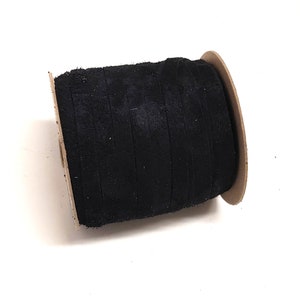 May include: A spool of black velvet ribbon. The ribbon is tightly wound on a cardboard spool, showcasing its soft, textured surface. The dark color of the ribbon contrasts with the white background, highlighting its rich texture. Ideal for crafting and sewing projects.