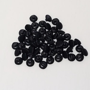 May include: A pile of black plastic buttons with a decorative design. The buttons are small and round, and they have a shiny finish.