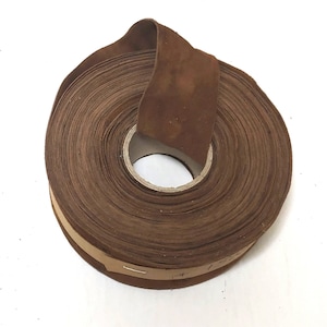 May include: A roll of brown leather cord, wound around a cardboard core. The leather is a dark brown colour and has a slightly rough texture.