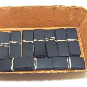 May include: A cardboard box filled with stacks of black rubber sheets, each stack secured with a rubber band.