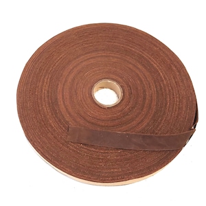 Może przedstawiać: Rolka brązowego skórzanego paska, zwinięta i gotowa do cięcia. Skóra ma bogaty brązowy kolor i naturalną, fakturowaną powierzchnię.