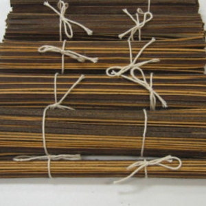 Puede incluir: Un paquete de listones de madera marrón y beige atados con cuerda blanca. Los listones miden aproximadamente 1,2 cm de ancho y 30 cm de largo.