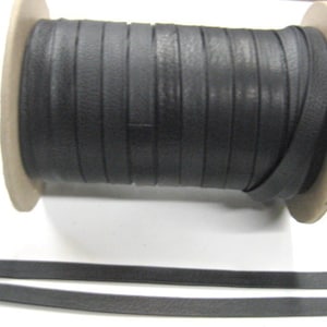 May include: A spool of black leather cord, wound around a cardboard core. The cord is approximately 1/4 inch wide and is shown unwound in the bottom of the image.