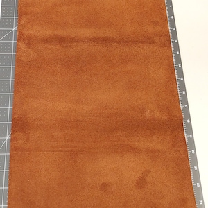 Puede incluir: Un trozo de cuero de gamuza marrón, que mide aproximadamente 25 cm por 35 cm.