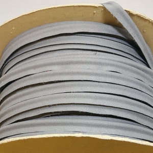 May include: A roll of grey bias binding, tightly wound. The binding is a solid, muted grey colour and appears to be made of fabric. The roll is made of cardboard. The binding is used for sewing and crafting.