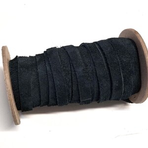 May include: A spool of black leather strips. The leather is tightly wound around a wooden spool, showcasing the texture and color of the material. The spool's wooden sides provide a natural contrast to the dark leather.