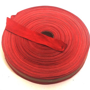 Può includere: Un rotolo di nastro di tessuto rosso con un bordo marrone. Il nastro è arrotolato e legato con un pezzo dello stesso nastro.