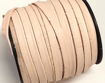 May include: A spool of light beige leather cord wrapped around a black plastic reel. The cord features a smooth, rounded top surface and flat, textured edges with visible vertical striations along the sides of the leather strip.