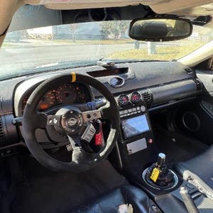 Op de afbeelding: Auto-interieur met dashboard, zwart stuur, meters en centraal scherm. Zwarte leren stoelen. De versnellingspook is zichtbaar.