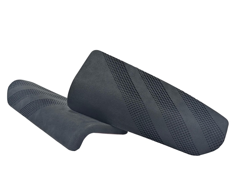 May include: Two dark gray shin guards with a textured surface and diagonal striped pattern. The guards are made of a flexible material and are designed to protect the lower legs during sports activities. The guards are shown against a white background.