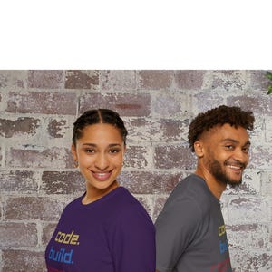 May include: Two people wearing t-shirts with the words "code. build. compete." printed on them. One shirt is purple, the other is gray. The background is a brick wall.