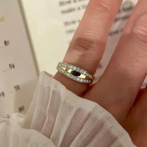 Puede incluir: Un anillo de oro y diamantes. El anillo presenta una banda central dorada flanqueada por hileras de pequeños diamantes brillantes. El diseño es simple pero elegante, adecuado para el uso diario o ocasiones especiales.
