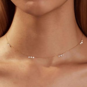 Può includere: Delicata collana d'oro con più piccole gemme scintillanti. La collana è infilata su una catena sottile, con le gemme disposte in gruppi e sparse lungo la scollatura. Il gioiello è mostrato su un collo.