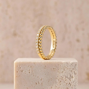 Könnte beinhalten: Ein goldener Ring mit einem Band, das auf einer Seite eine Reihe kleiner, runder, polierter Goldperlen und auf der anderen Seite eine Reihe winziger, klarer, funkelnder Diamanten im Rundschliff in einer Goldfassung aufweist.