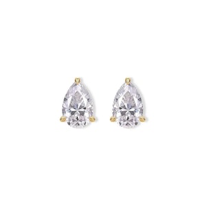 May include: A pair of gold-colored stud earrings, each featuring a pear-shaped, clear gemstone. The gemstones are held in place by three gold prongs, creating a classic and elegant look. The earrings are set against a white background.