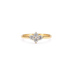 May include: A gold ring featuring a cluster of four round, clear, faceted stones arranged in a diamond-shaped pattern at the centre. The band is smooth and polished, with the stones held in place by small metal prongs on a gold setting.