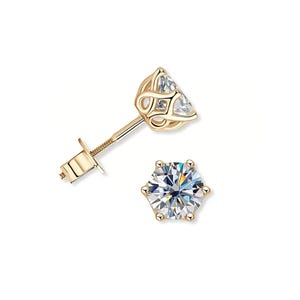 May include: Two gold-coloured stud earrings, each featuring a clear, faceted gemstone. One earring is shown from the side, displaying the post and detailed setting. The other is viewed from the front, highlighting the gemstone's sparkle. Jewellery.