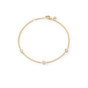 Può includere: Un delicato bracciale a catena color oro con tre pietre rotonde e trasparenti incastonate a lunetta, distanziate uniformemente. Il bracciale presenta una sottile catena a maglie, una chiusura a moschettone e un piccolo ciondolo circolare.