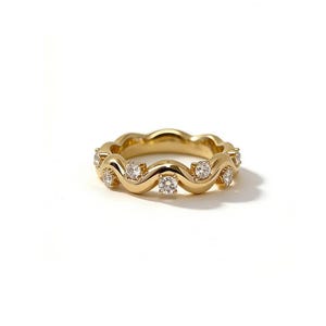 May include: A gold ring with a wavy design, set with multiple clear gemstones. The ring is made of polished gold and features a repeating pattern of curves, each holding a sparkling stone. The ring is displayed on a white background.