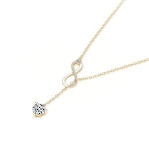 May include: A gold-colored necklace featuring an infinity symbol adorned with small, clear gemstones. A larger, round, clear gemstone hangs from the bottom of the infinity symbol. The necklace is on a white background.