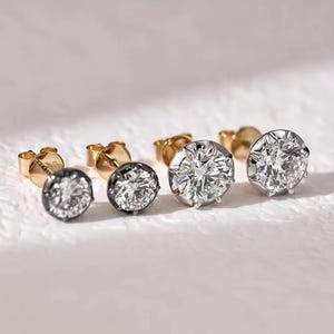 Può includere: Quattro orecchini a lobo dal taglio rotondo disposti in fila. I due orecchini più piccoli a sinistra presentano montature in metallo scuro annerito, mentre i due più grandi a destra sono incastonati in metallo color argento lucido con perno dorato.
