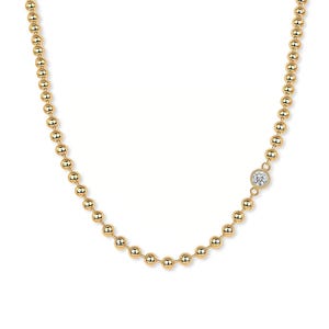 Può includere: Una delicata collana d'oro con una catena di piccole perle rotonde. Un singolo diamante scintillante è incastonato in una lunetta sul lato della collana, aggiungendo un tocco di eleganza al design.