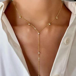 May include: A delicate gold-toned necklace with a Y-shaped pendant design. The necklace features small, sparkling cubic zirconia stones evenly spaced along the chain and pendant. The necklace is shown against a white button-down shirt.