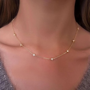 May include: A delicate gold necklace featuring multiple small, round, clear gemstones evenly spaced along the chain. The necklace is worn around the neck, with the gemstones catching the light.