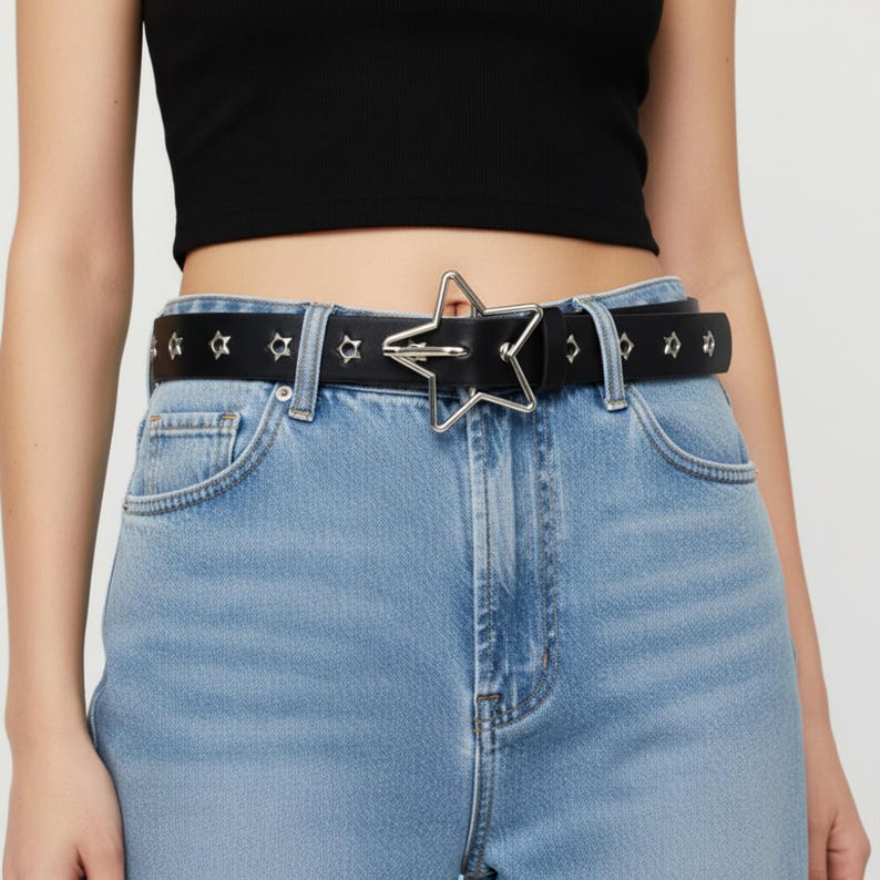 May include: Black belt with a silver star-shaped buckle. The belt is made of leather and has small star-shaped studs along its length. The belt is worn with blue jeans and a black top.