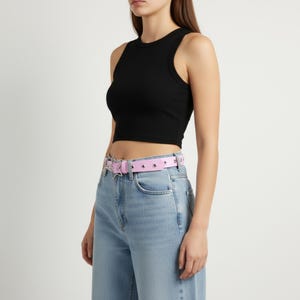May include: A black ribbed crop top paired with light blue jeans and a pink belt. The belt features silver-colored star and stud embellishments. The outfit is simple and stylish.