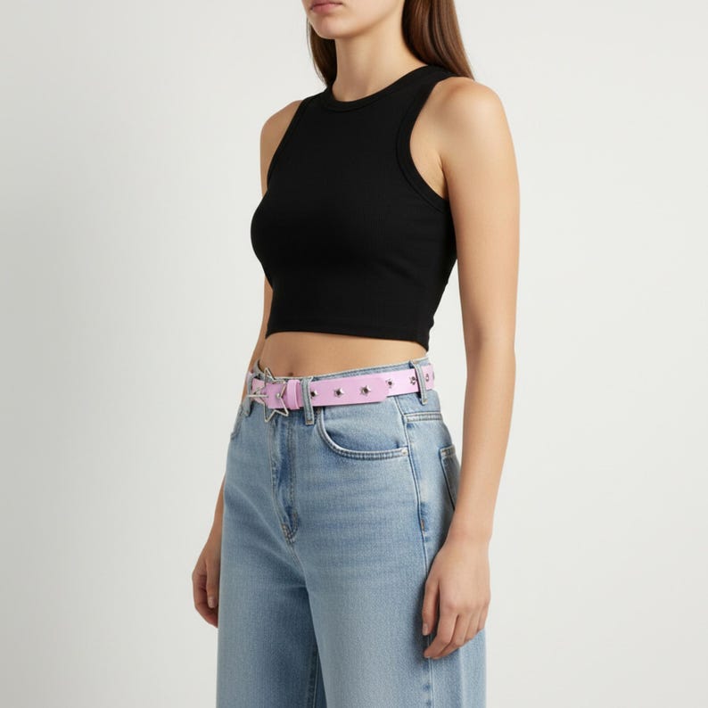 May include: A black ribbed crop top paired with light blue jeans and a pink belt. The belt features silver-colored star and stud embellishments. The outfit is simple and stylish.