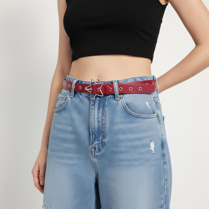 May include: A red belt with star-shaped cutouts and a silver star-shaped buckle. The belt is worn with light blue denim jeans. The jeans have distressed details.